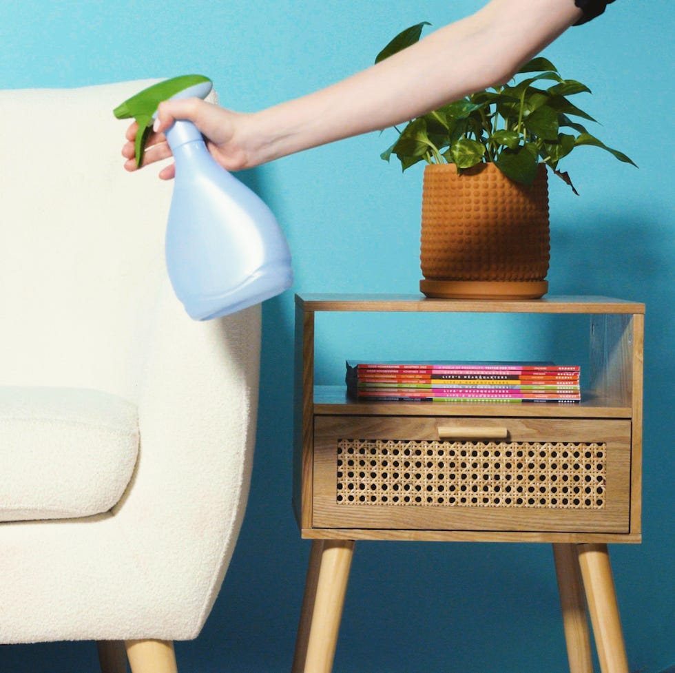 spraying febreze on cream colored fabric couch